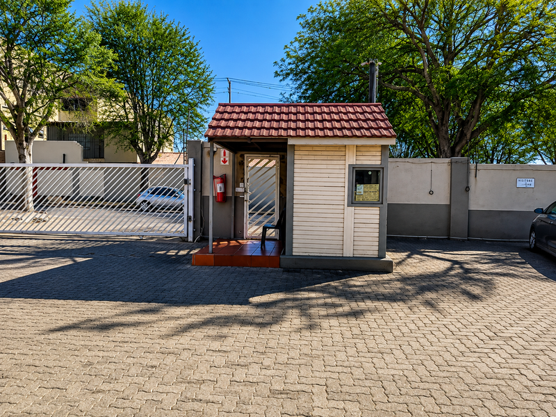 A secure entrance area featuring a guard house, paved driveway, and perimeter wall with a sliding gate for controlled access.