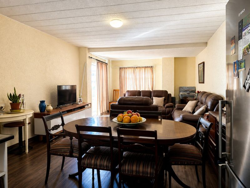 Spacious open-plan living and dining area featuring laminate flooring, textured ceilings, and direct access to an outdoor space through sliding glass doors.