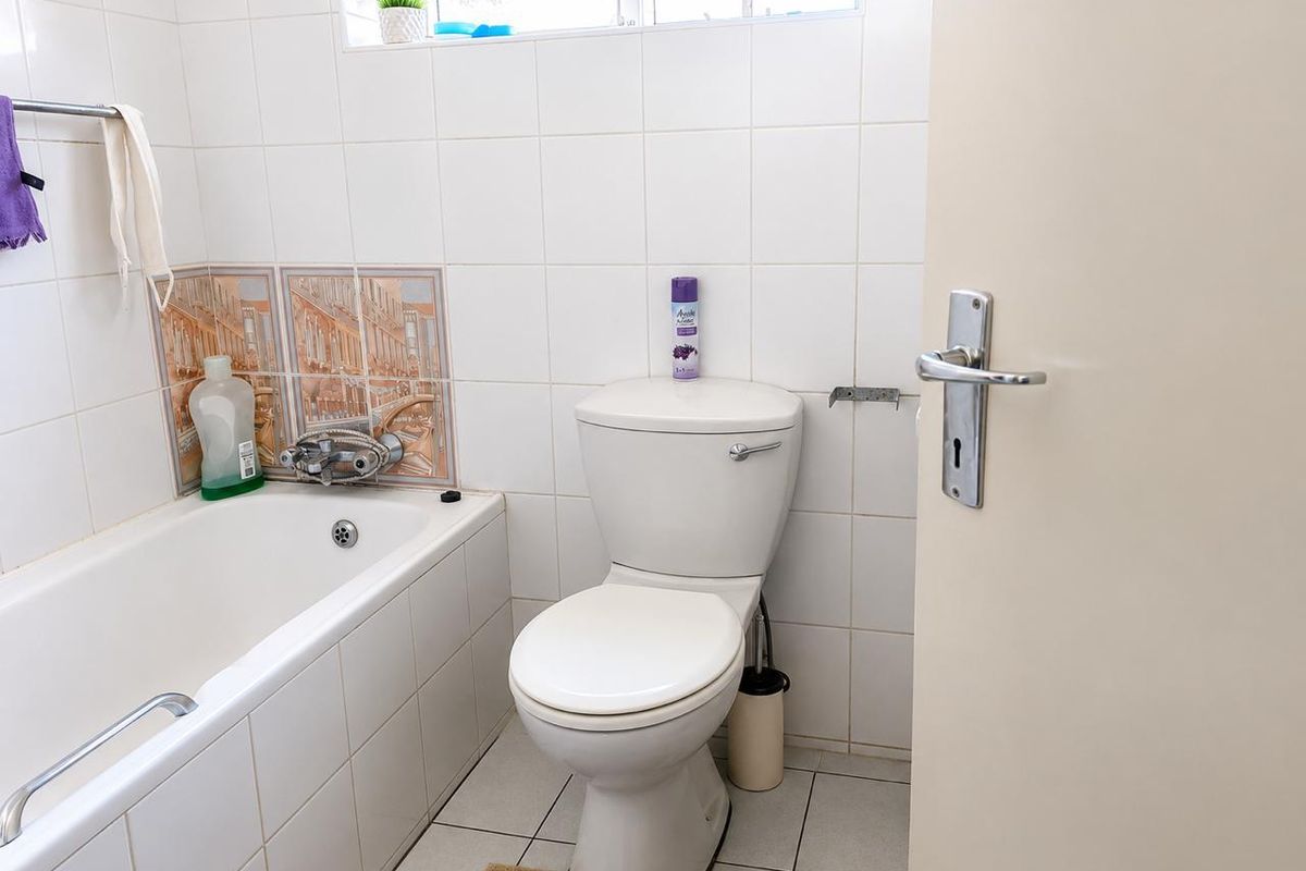 A functional bathroom featuring a bathtub with a mixer tap, a standard toilet, and white wall tiling.