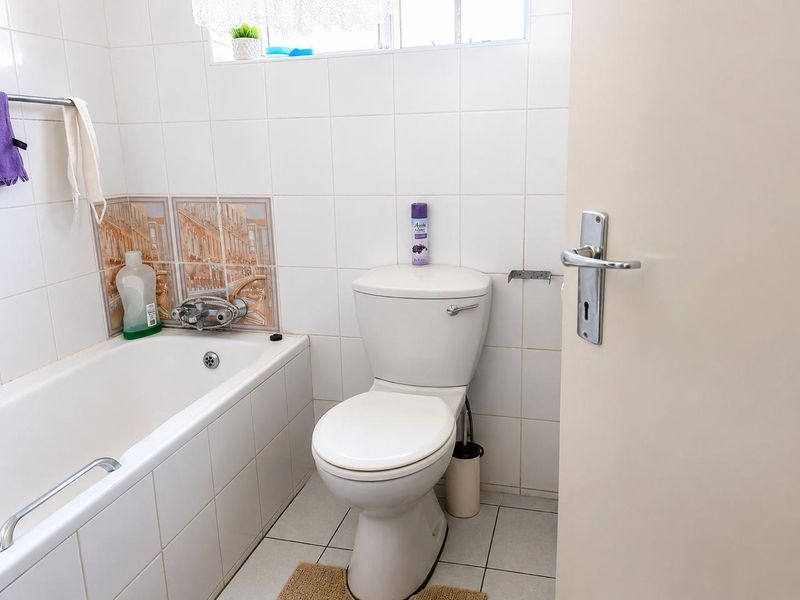 A functional bathroom featuring a bathtub with a mixer tap, a standard toilet, and white wall tiling.