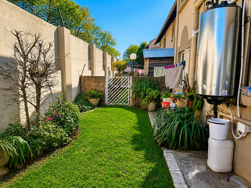 A private rear garden featuring a well-maintained lawn, perimeter wall with electric fencing, and an external geyser unit.