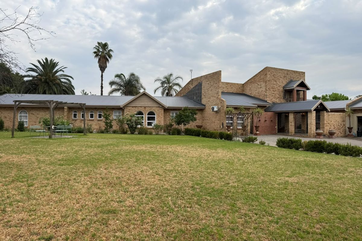 Spacious rear exterior view of a face brick house featuring a metal roof, arched windows, and a large landscaped garden with a pergola.