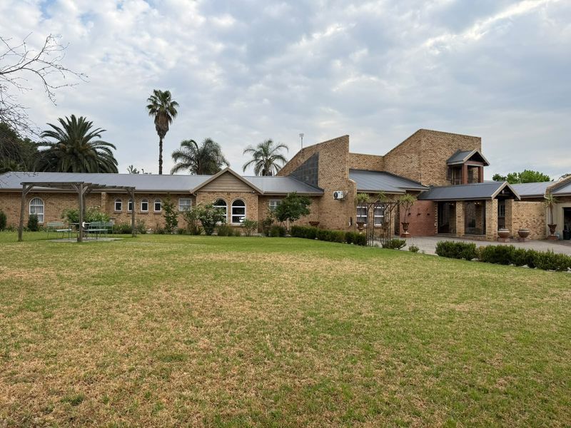 Spacious rear exterior view of a face brick house featuring a metal roof, arched windows, and a large landscaped garden with a pergola.