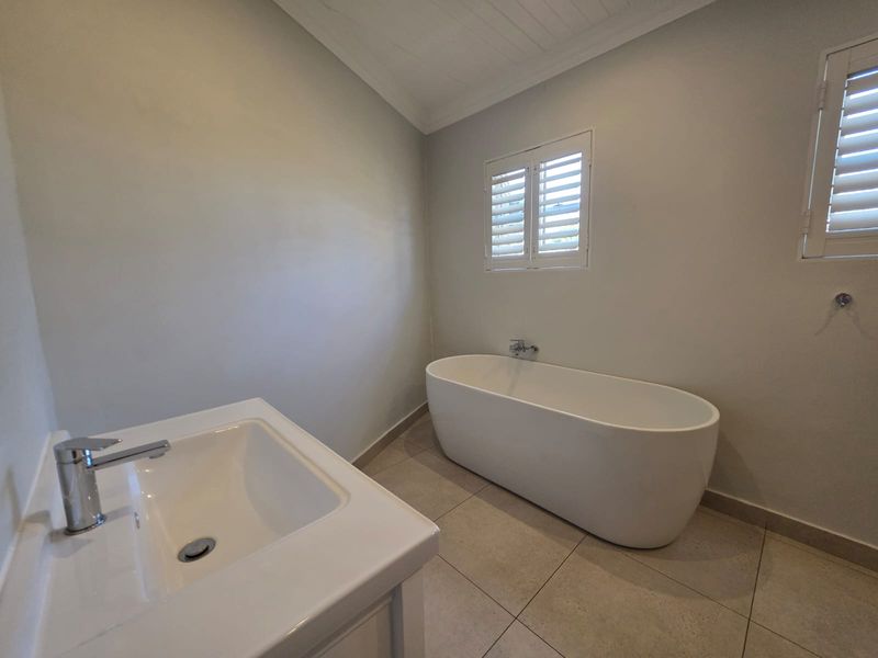 A clean and modern bathroom featuring a freestanding bathtub, vanity basin with mixer tap, and plantation shutters on the windows.