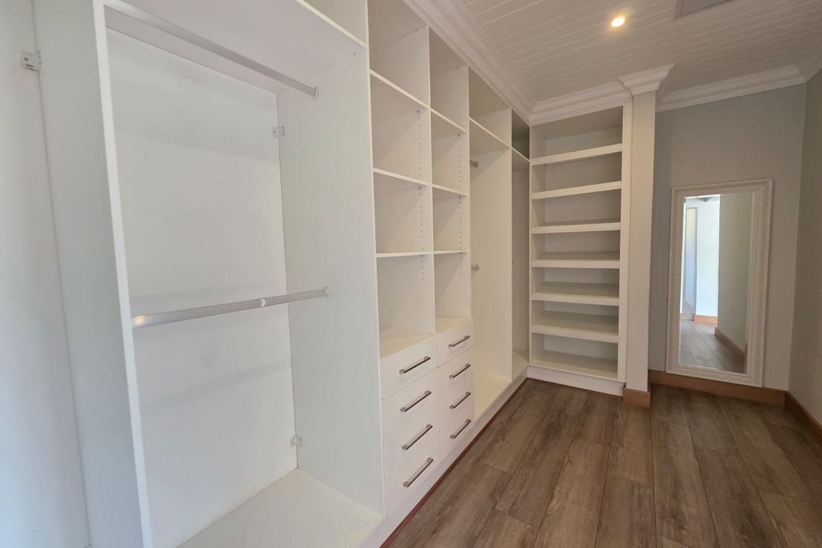 A spacious walk-in closet featuring extensive built-in cabinetry, shelving, hanging rails, and drawers, complemented by timber-look flooring and a classic beadboard ceiling.