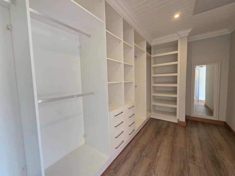 A spacious walk-in closet featuring extensive built-in cabinetry, shelving, hanging rails, and drawers, complemented by timber-look flooring and a classic beadboard ceiling.