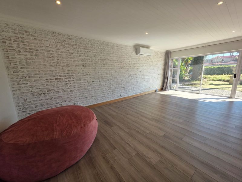 Spacious living room featuring a white-washed exposed brick wall, timber laminate flooring, split system air conditioning, and large sliding doors opening to the garden.