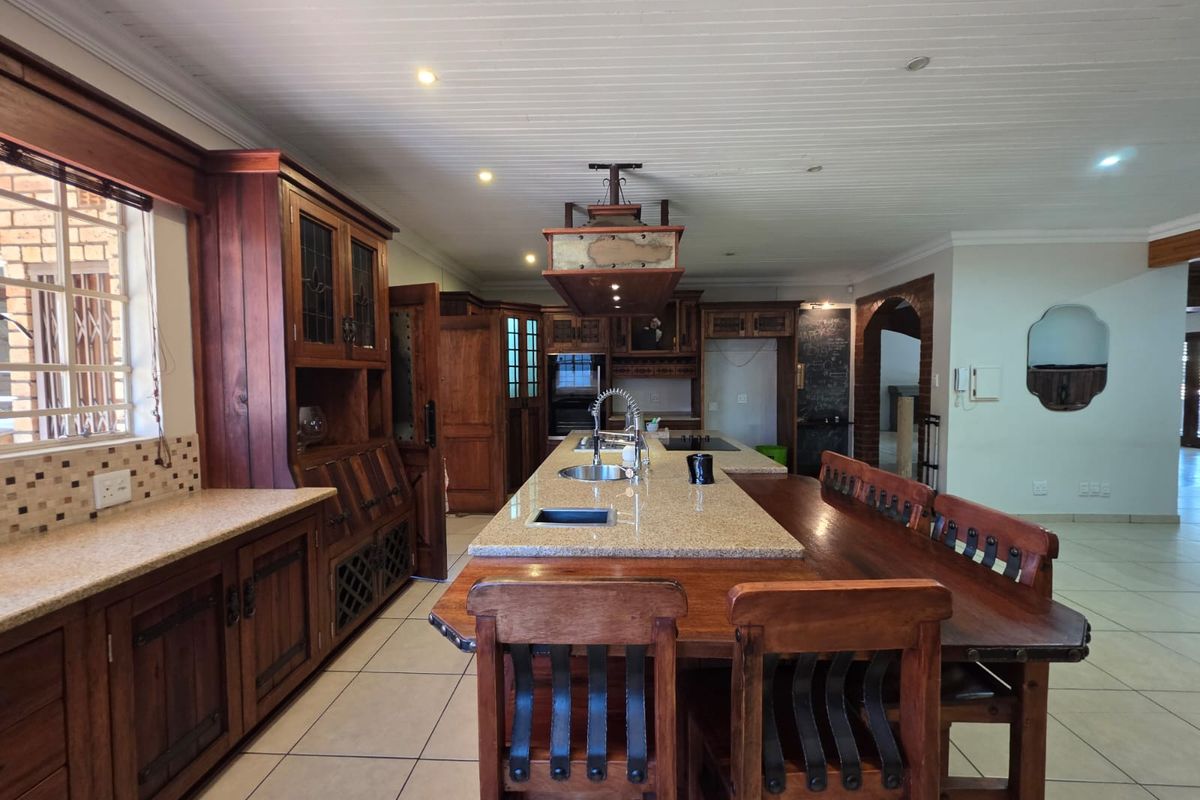 Spacious kitchen featuring extensive wooden cabinetry, a large central island with granite countertops, integrated appliances, and tiled flooring.