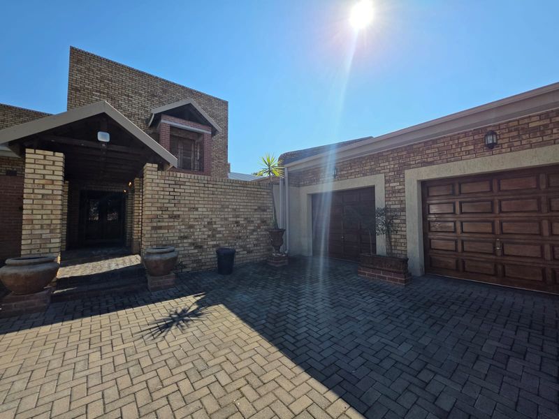 Front exterior view of the house featuring a brick facade, paved driveway, and a double garage with wooden doors.