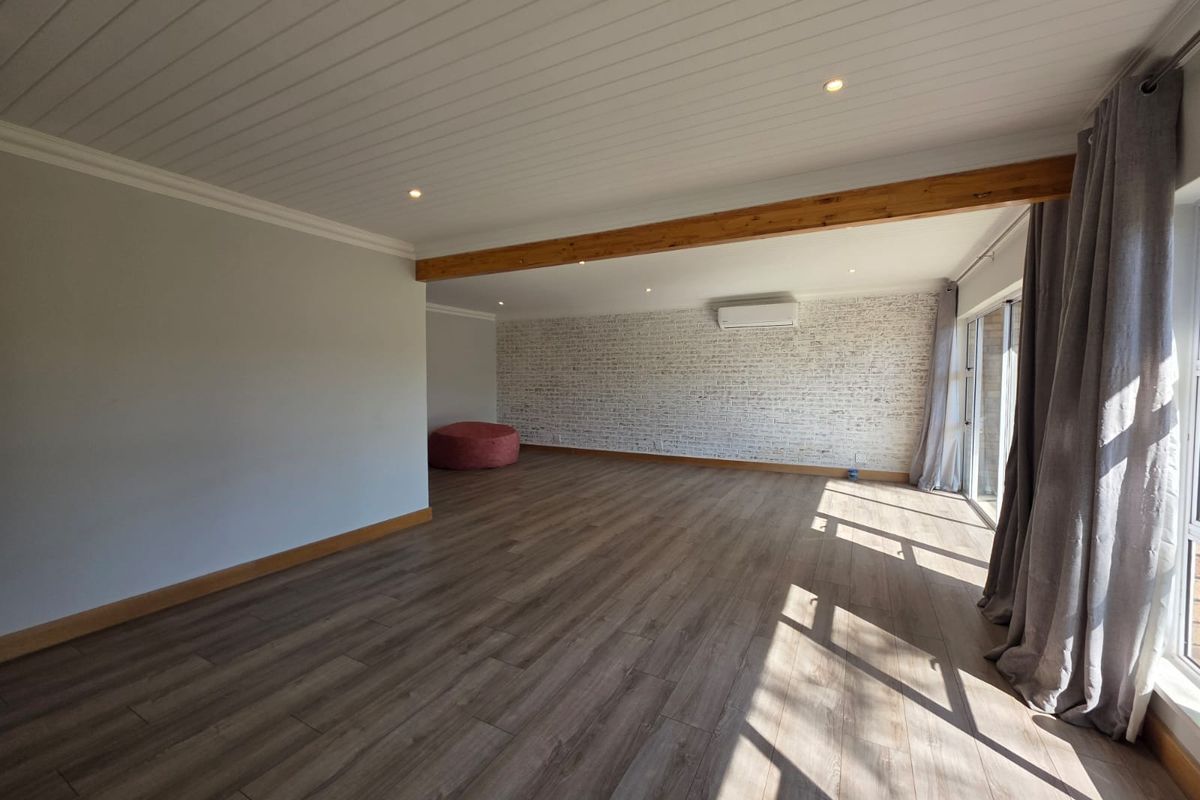 Spacious living area featuring timber beam accents, exposed brick feature wall, laminate flooring, and a split-system air conditioner.