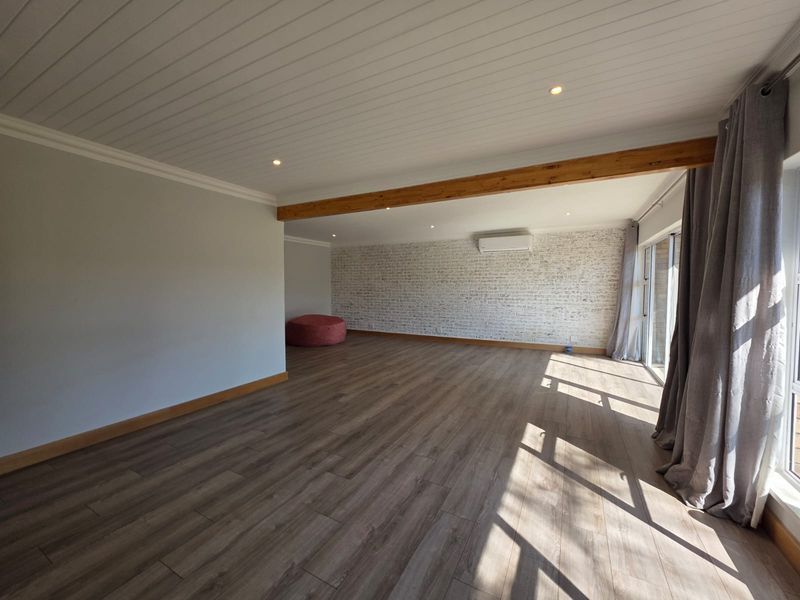 Spacious living area featuring timber beam accents, exposed brick feature wall, laminate flooring, and a split-system air conditioner.