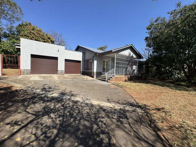 Front view of a residential property featuring a double garage with roller shutter doors, a paved driveway, and a covered entrance porch with security gates.
