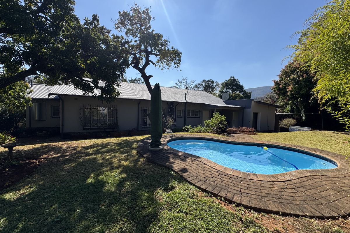 Rear view of the property featuring a swimming pool with brick coping, a metal roof, and a spacious garden area.