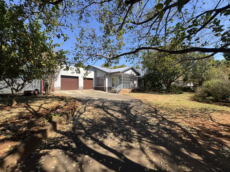 Front view of a single-story house featuring a double garage, paved driveway, and established garden with mature trees.