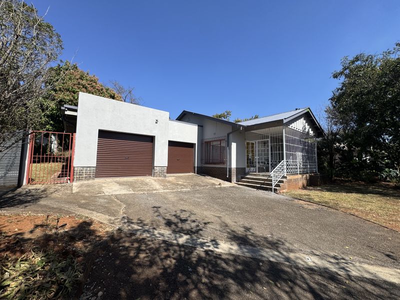 Front elevation of a house featuring a double garage with roller doors, a paved driveway, and a covered porch with security gates.