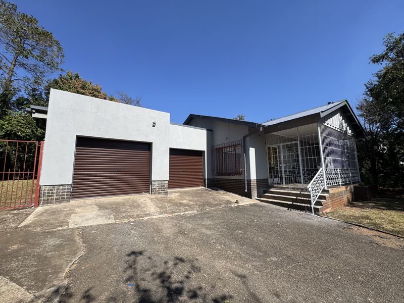 Front exterior view of a house featuring a double garage with roller shutter doors, a paved driveway, and a covered porch with security bars.