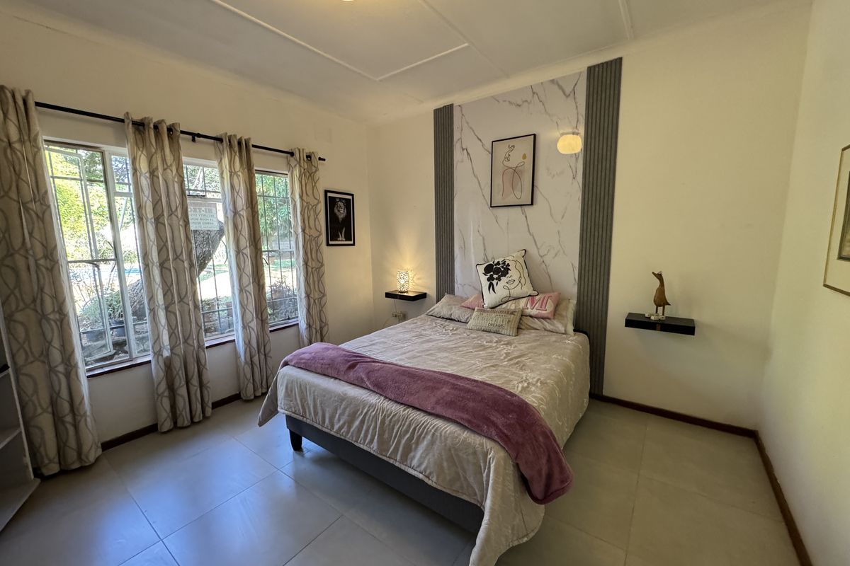 A well-lit bedroom featuring tiled flooring, large windows, and a decorative marble-effect feature wall with integrated floating bedside shelves.