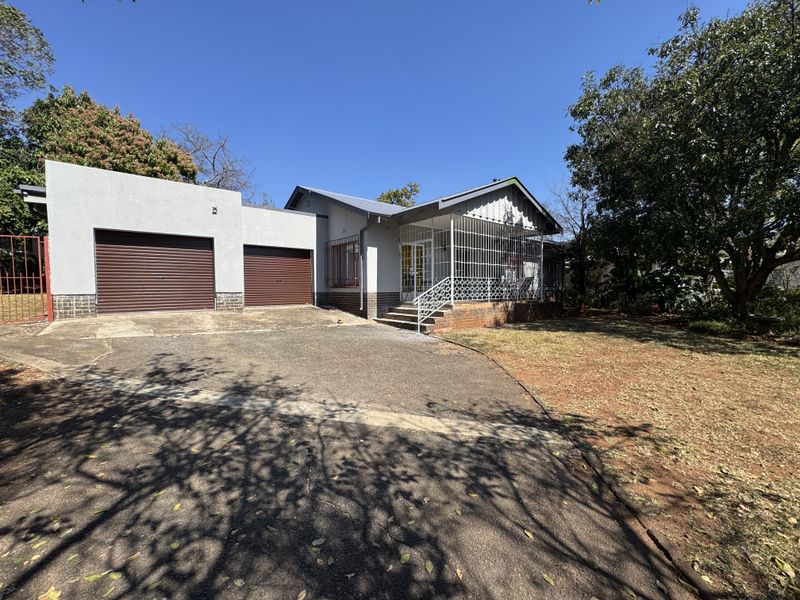 Front view of a single-story house featuring a double garage with roller doors, a paved driveway, and a covered porch with security gates.