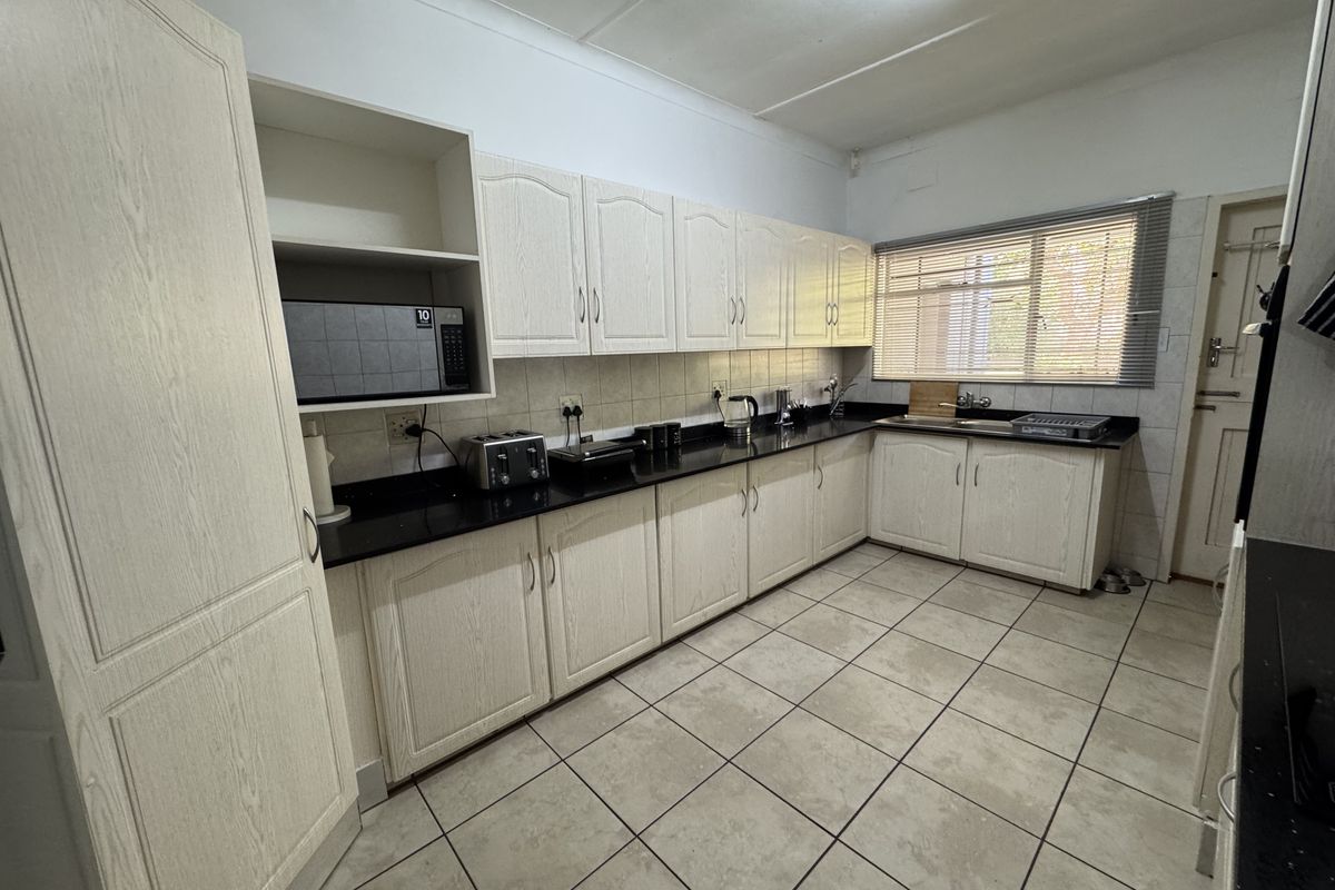 A functional kitchen featuring light wood-grain cabinetry, dark granite countertops, tiled flooring, and a tiled backsplash with ample storage space.