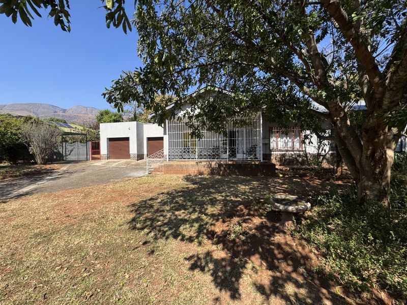 Front view of a single-story house featuring a brick driveway, garage access, and a covered porch with security bars, set on a spacious garden lot.