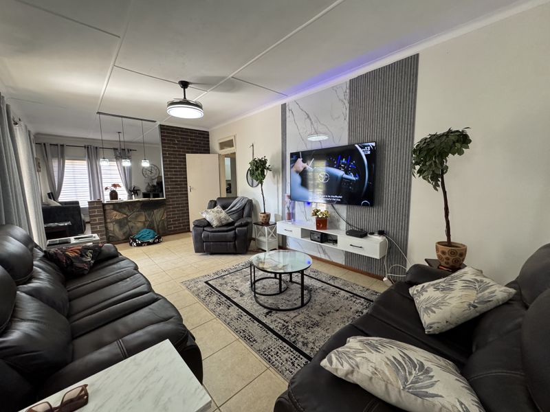 A well-maintained living room featuring tiled floors, a modern feature wall with marble and slatted accents, and a stone-clad breakfast bar.