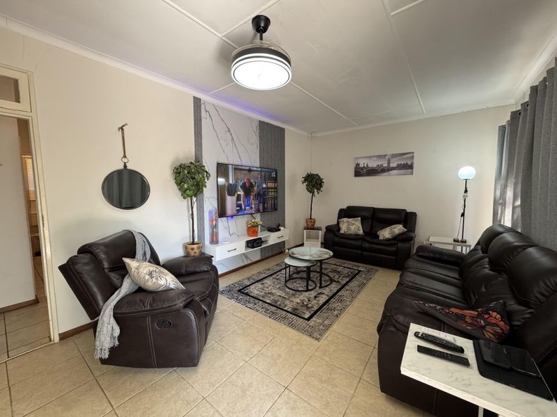 A comfortable living room featuring tiled flooring, a modern ceiling fan, and a decorative feature wall panel behind the television area.