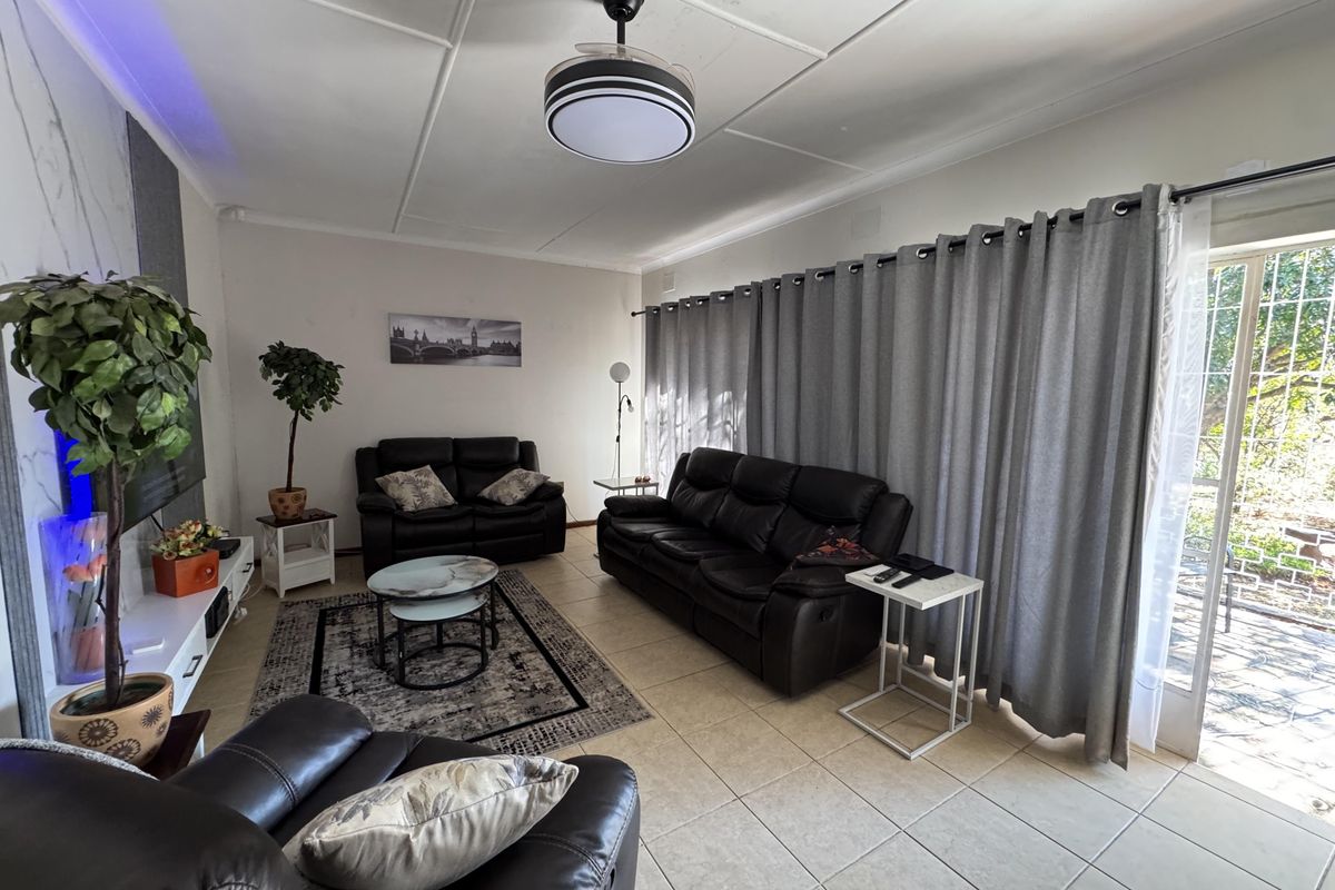 A comfortable living room featuring tiled flooring, a modern ceiling fan, and a large sliding glass door providing access to the outdoor area.