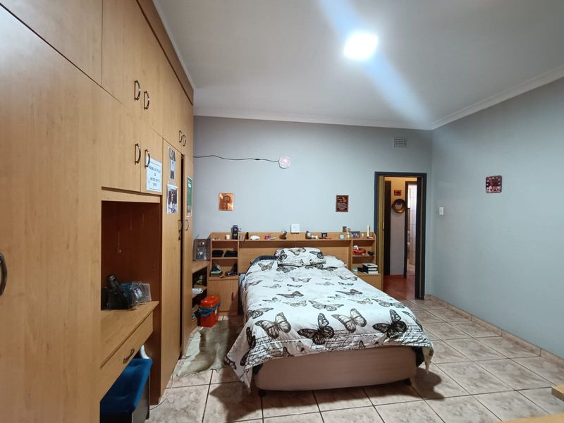 A bedroom featuring built-in wooden cupboards, tiled flooring, and a neutral wall finish, providing a functional and well-proportioned living space.