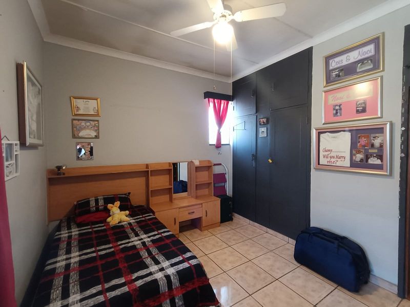 A bedroom featuring tiled flooring, a ceiling fan, and dark-painted built-in cupboards providing ample storage space.