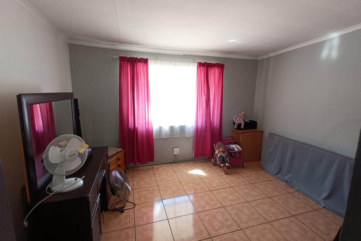 A standard bedroom featuring neutral wall paint, tiled flooring, and a central window with curtain fixtures.