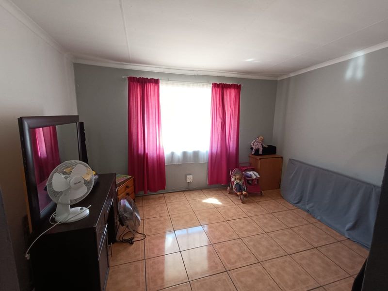 A standard bedroom featuring neutral wall paint, tiled flooring, and a central window with curtain fixtures.