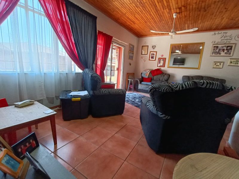 A living room featuring tiled flooring, a timber tongue and groove ceiling, a ceiling fan, and access to an outdoor area via a sliding door.