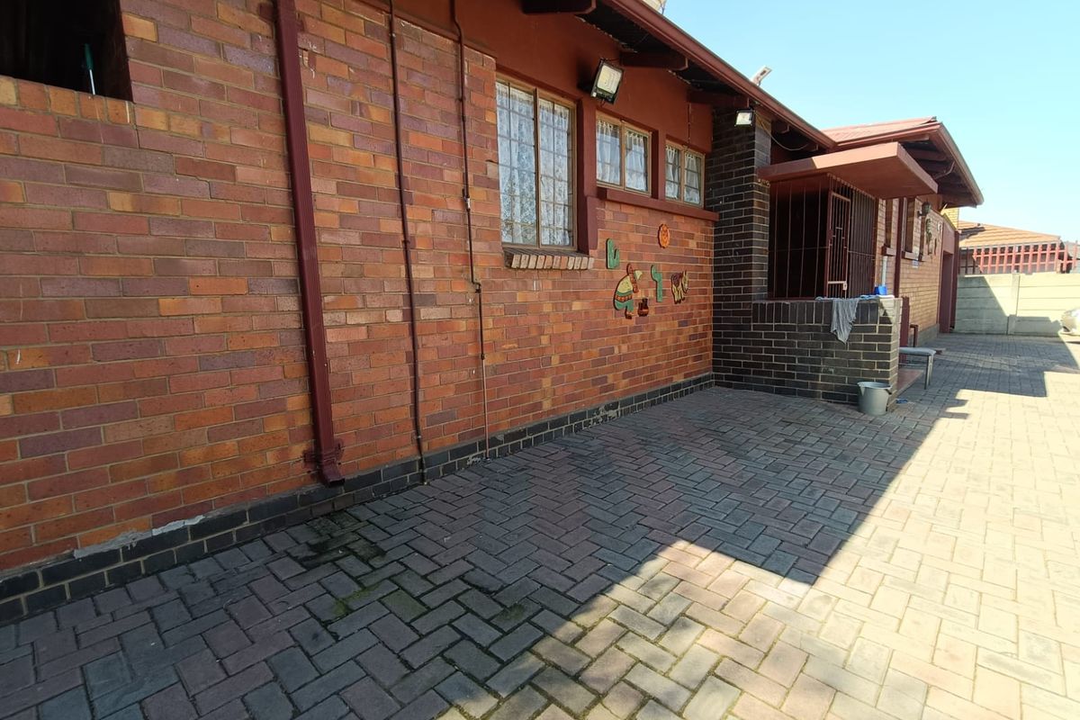 Rear exterior view of the house featuring a brick facade, paved patio area, and security bars on the windows.