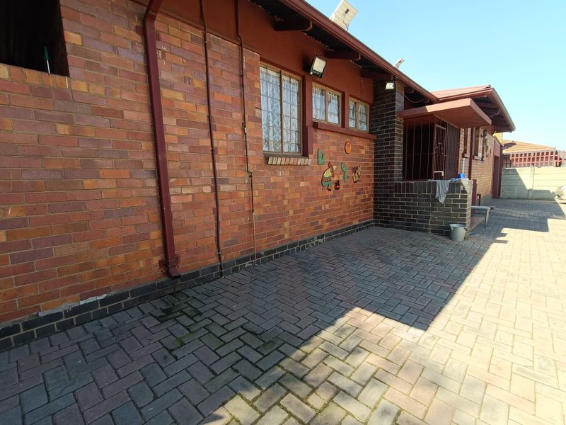 Rear exterior view of the house featuring a brick facade, paved patio area, and security bars on the windows.