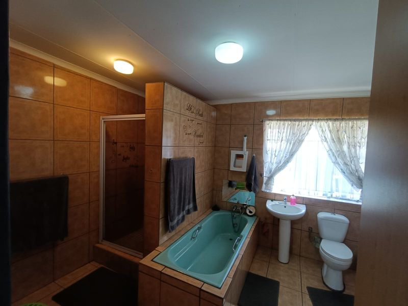 A functional bathroom featuring a built-in bathtub, separate shower enclosure, pedestal basin, and toilet, finished with full-height wall tiling.