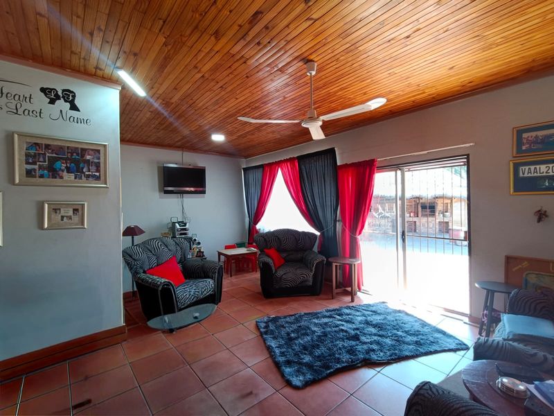 A living room featuring a timber-clad ceiling, ceiling fan, tiled flooring, and a sliding glass door providing access to the exterior.