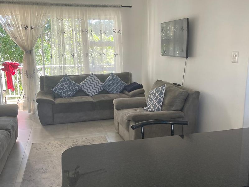 Open plan living area featuring tiled floors, a ceiling fan, and a breakfast bar with granite countertop, leading to a balcony.