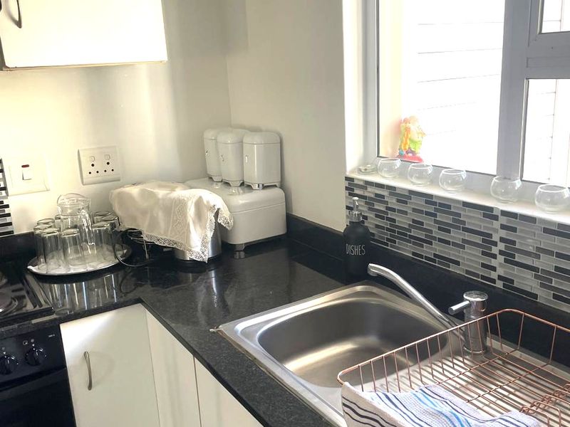 A functional kitchen featuring white cabinetry, dark granite countertops, a mosaic tile backsplash, and a stainless steel sink with a modern mixer tap.