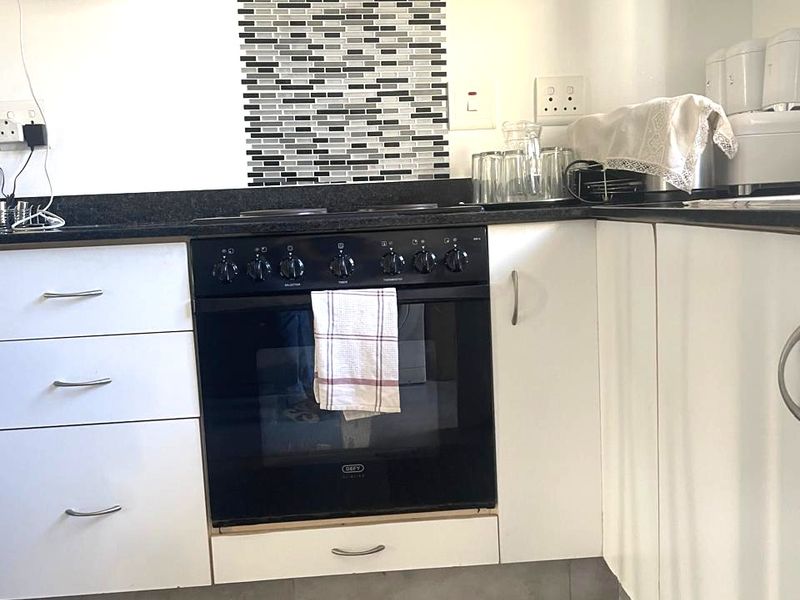 Compact kitchen featuring white cabinetry, black granite countertops, a mosaic tile splashback, and a built-in oven with an overhead extractor fan.