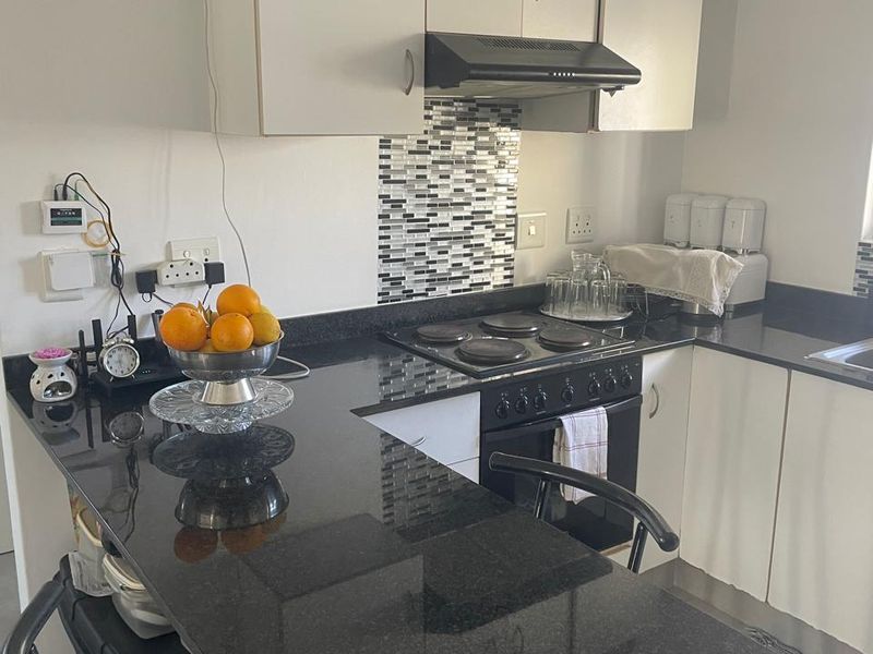 Compact kitchen featuring black granite countertops, mosaic tile backsplash, built-in electric hob, oven, and white cabinetry with integrated extractor fan.