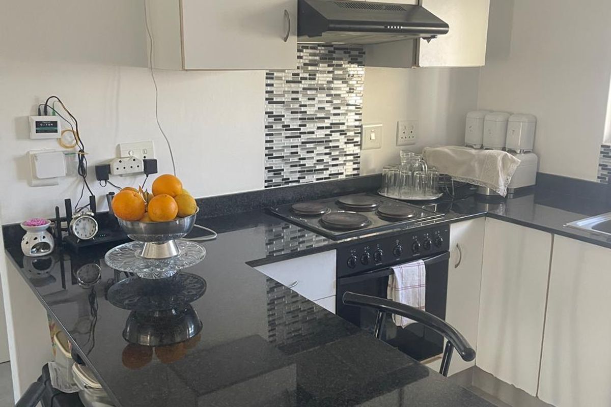Compact kitchen featuring black granite countertops, mosaic tile backsplash, built-in electric hob, oven, and white cabinetry with integrated extractor fan.