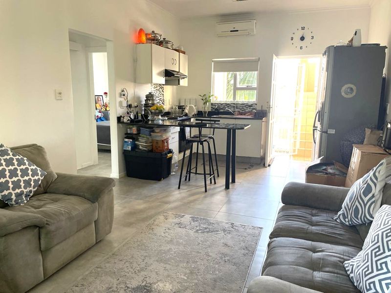 Open-plan living and kitchen area featuring tiled floors, granite countertops, built-in cabinetry, and a split-system air conditioner with direct access to an outdoor space.