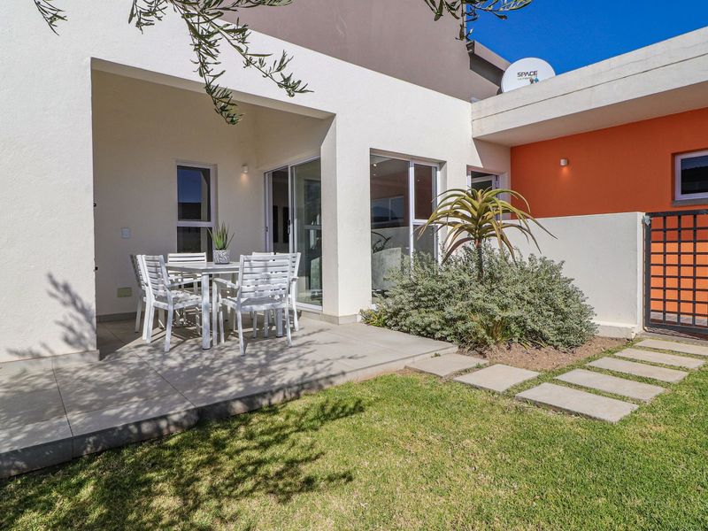 A well-maintained covered patio area featuring tiled flooring and sliding glass doors, leading out to a neat garden with a paved walkway.