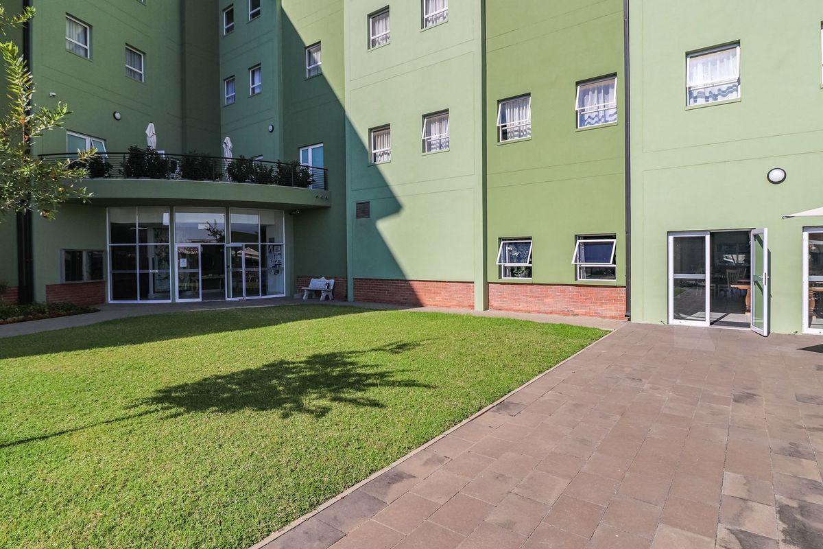 A rear exterior view of the building featuring a paved patio area, a well-maintained lawn, and access to the interior via sliding glass doors.