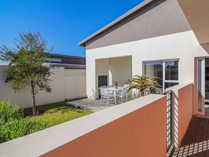 A well-maintained covered patio featuring a built-in braai, overlooking a private garden area with paved flooring and direct access to the interior living space.