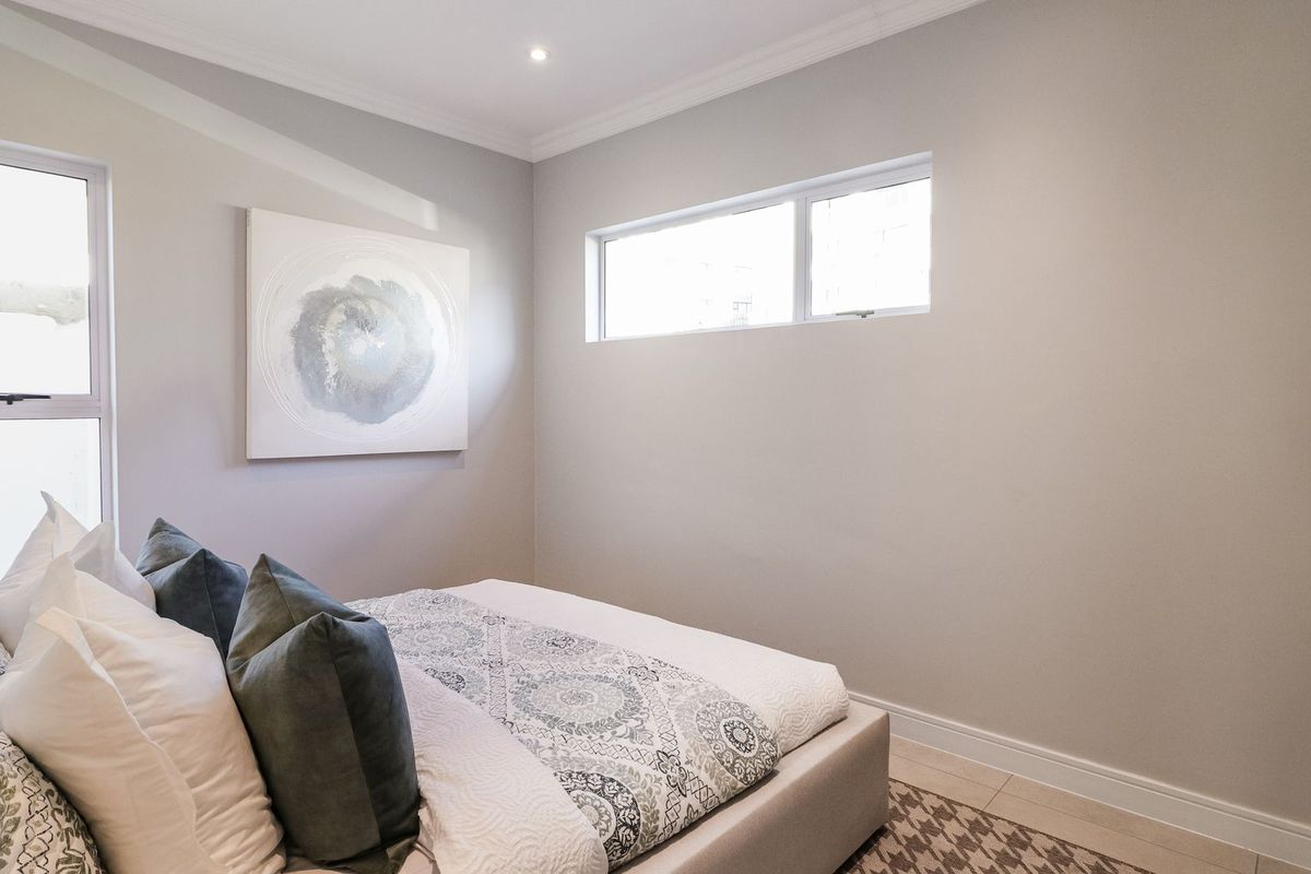 A well-maintained bedroom featuring neutral wall tones, tiled flooring, recessed downlighting, and decorative cornicing.