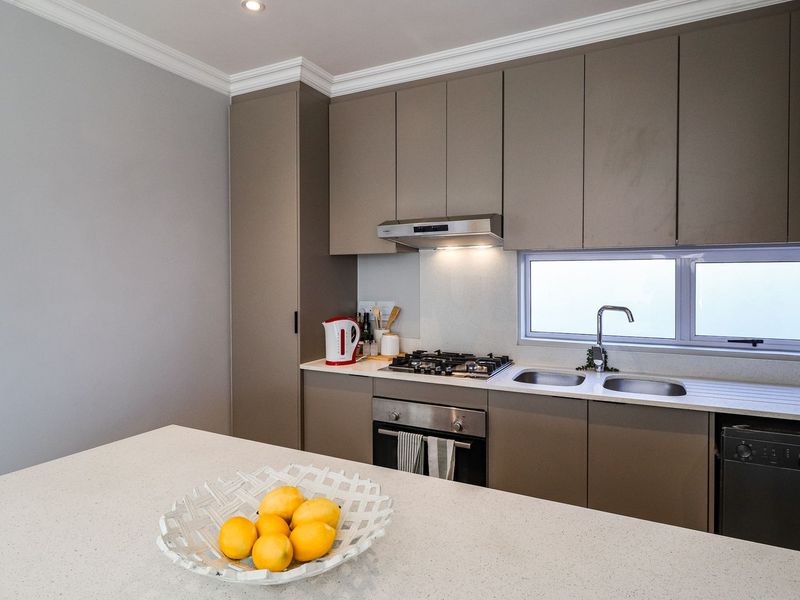 Modern kitchen featuring sleek taupe cabinetry, stone countertops, gas cooktop, built-in oven, and integrated dishwasher with a clean, contemporary finish.