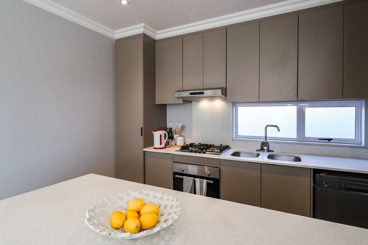 Modern kitchen featuring sleek taupe cabinetry, stone countertops, gas cooktop, built-in oven, and integrated dishwasher with a clean, contemporary finish.