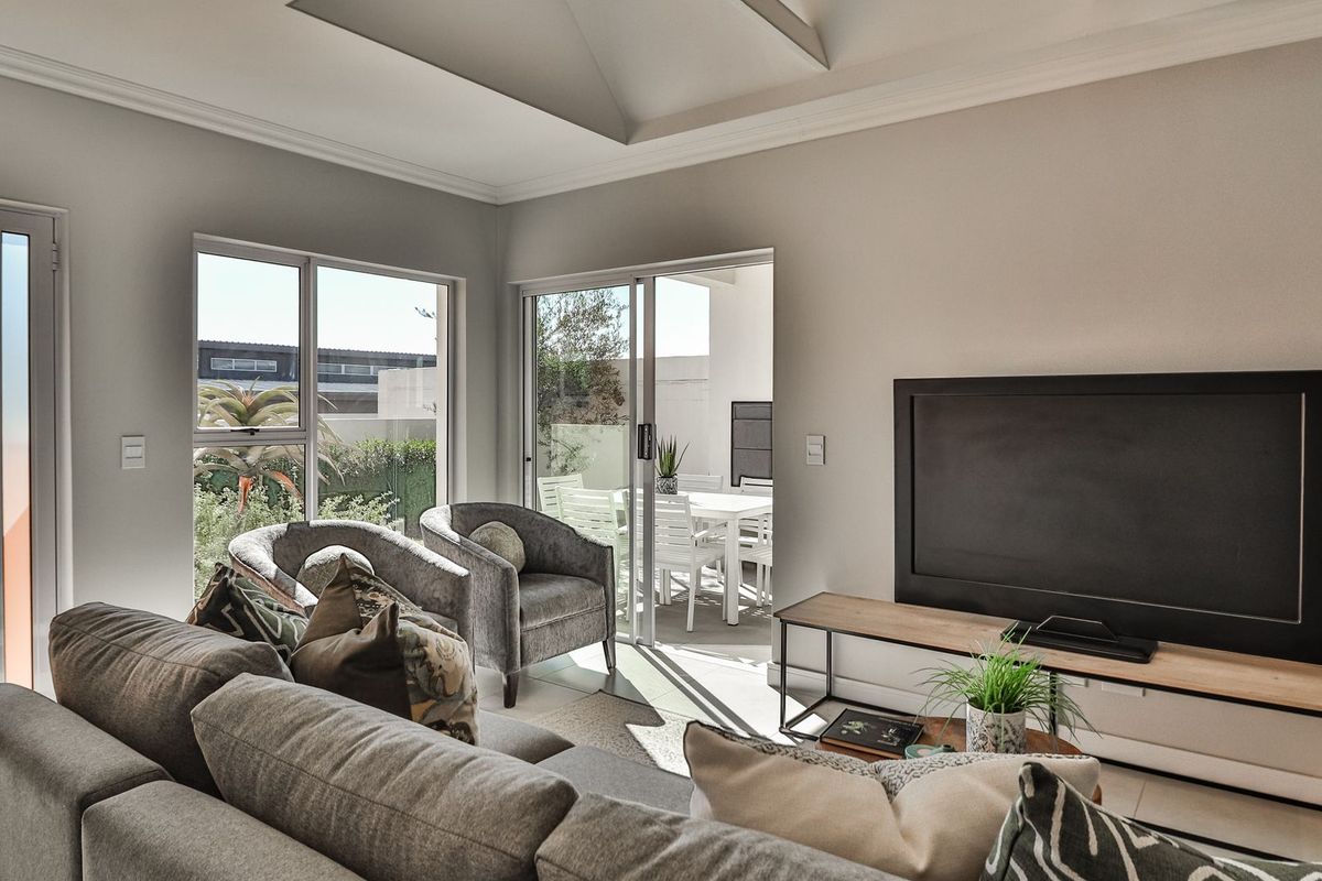 Bright living room featuring a tray ceiling, tiled flooring, and large sliding glass doors providing seamless access to the outdoor patio area.