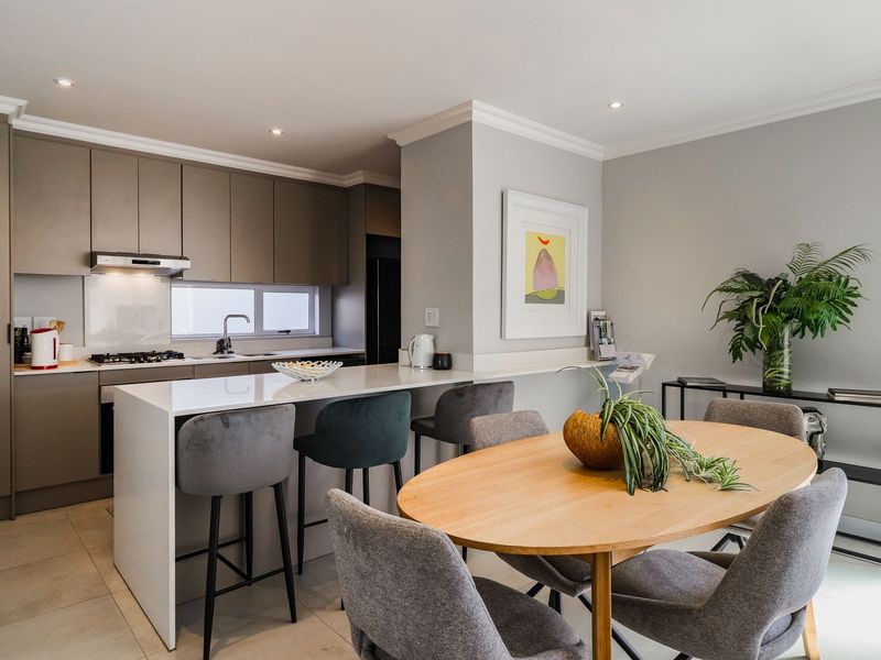 Modern open-plan kitchen and dining area featuring sleek cabinetry, stone countertops, integrated appliances, and recessed lighting, creating a functional and contemporary living space.